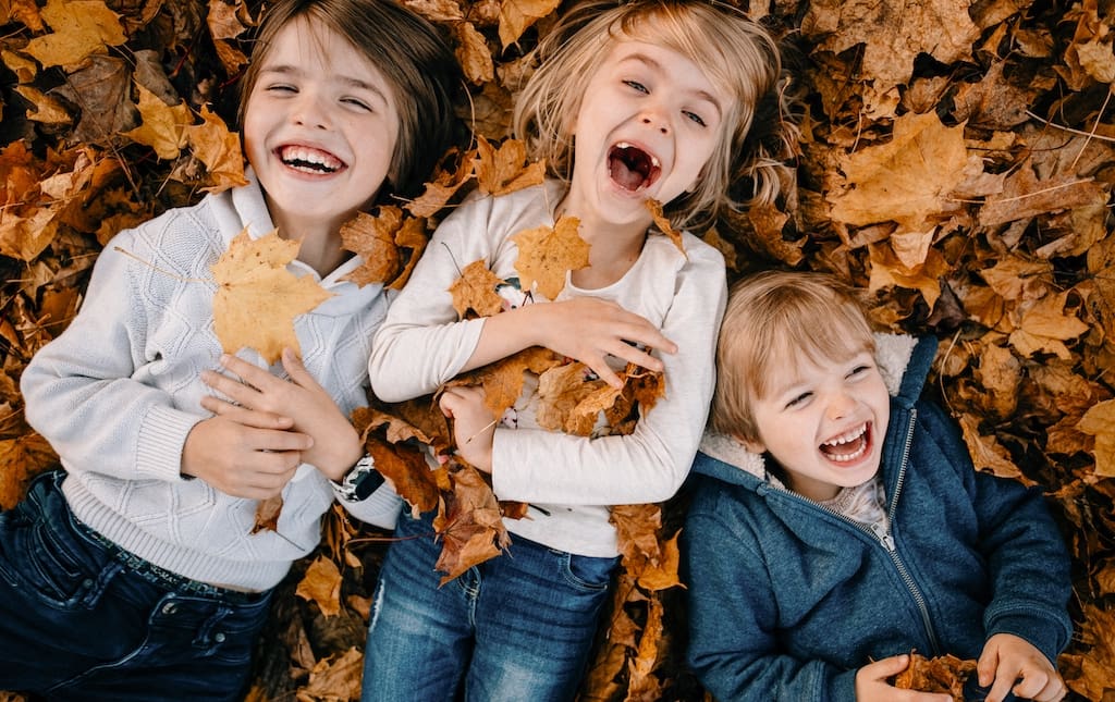 Children enjoying the fall season lying in a pile of leaves