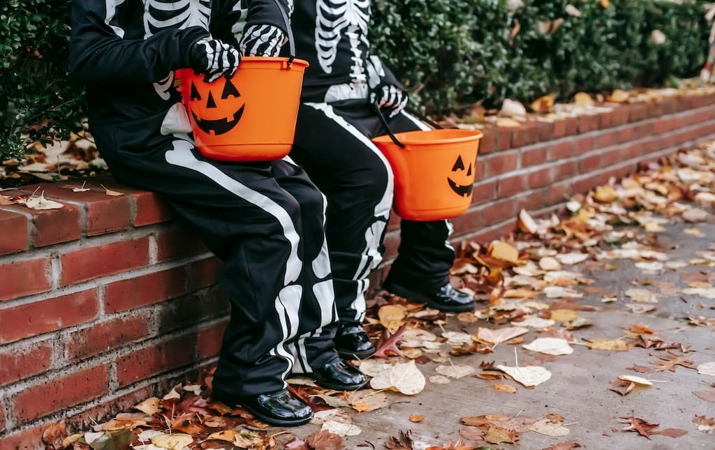 two kids sitting on a brick ledge in skeleton halloween costumes