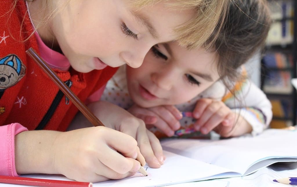 Two young girls writing on a school worksheet