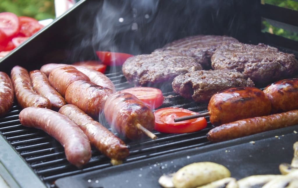 Hot dogs and hamburgers sizzling on a grill outside