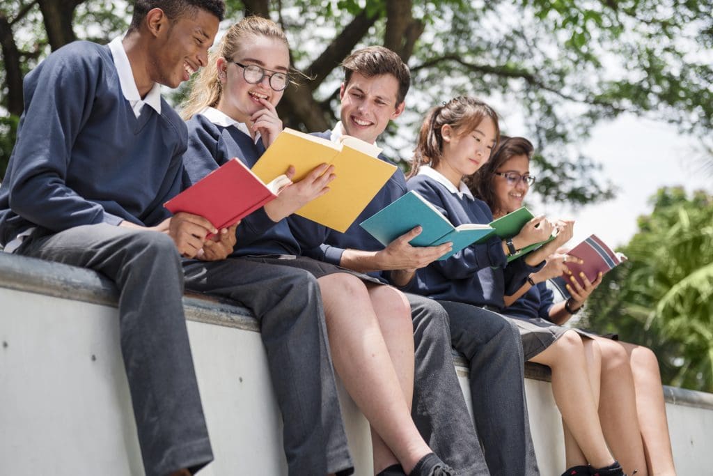 Teenage students sit outside a school reading during a read-a-thon.