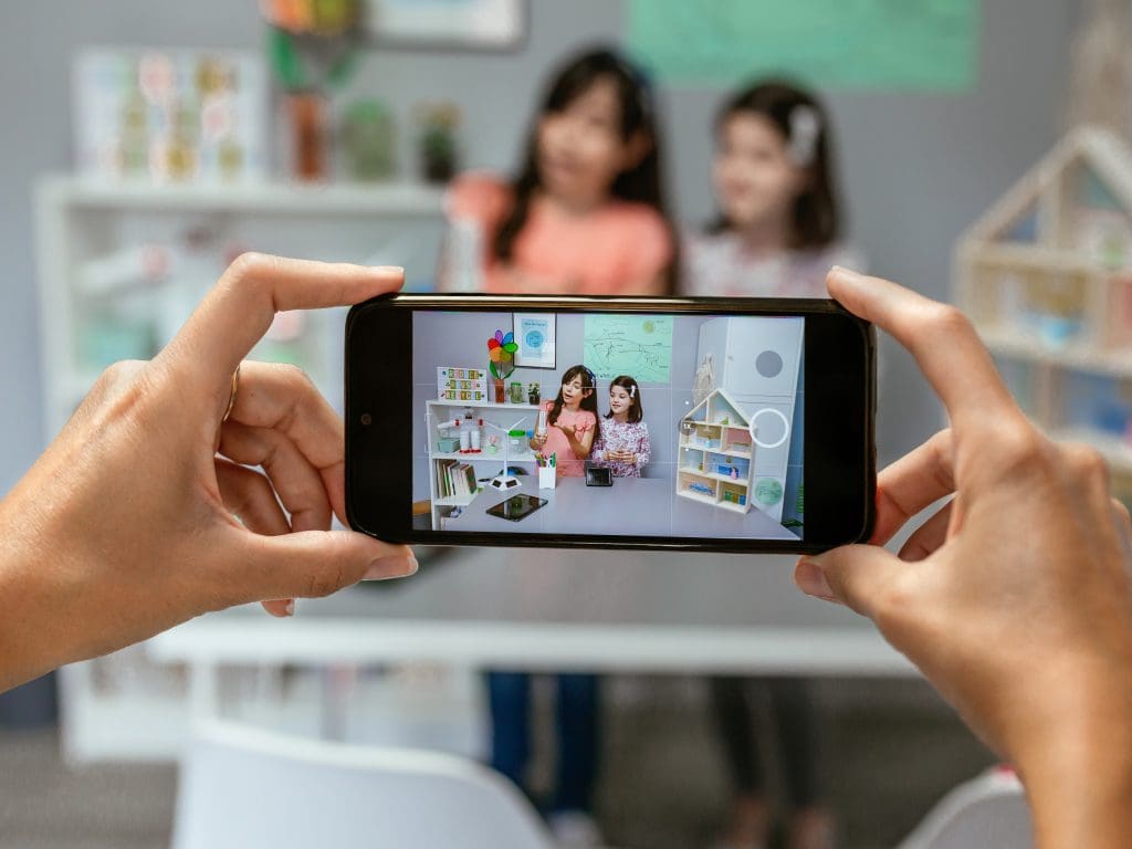 A teacher records a TikTok video of two students presenting their project on recycling in class.