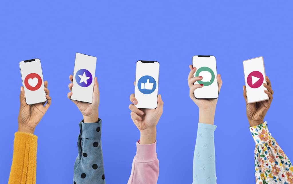 Five children's arms raise holding up smartphones each displaying a different social media icon against a white background