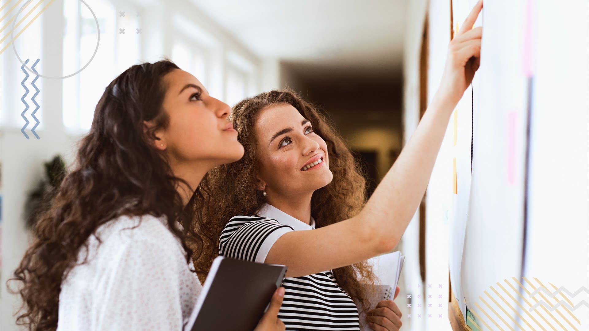 Two students looking at canva flyers hanging on a bulletin board at school