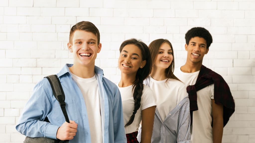 Smiling high school students standing against white brick wall in school after successful fundraiser